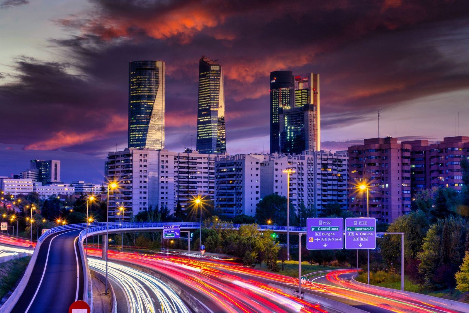 Avenida iluminada frente a un distrito financiero al anochecer